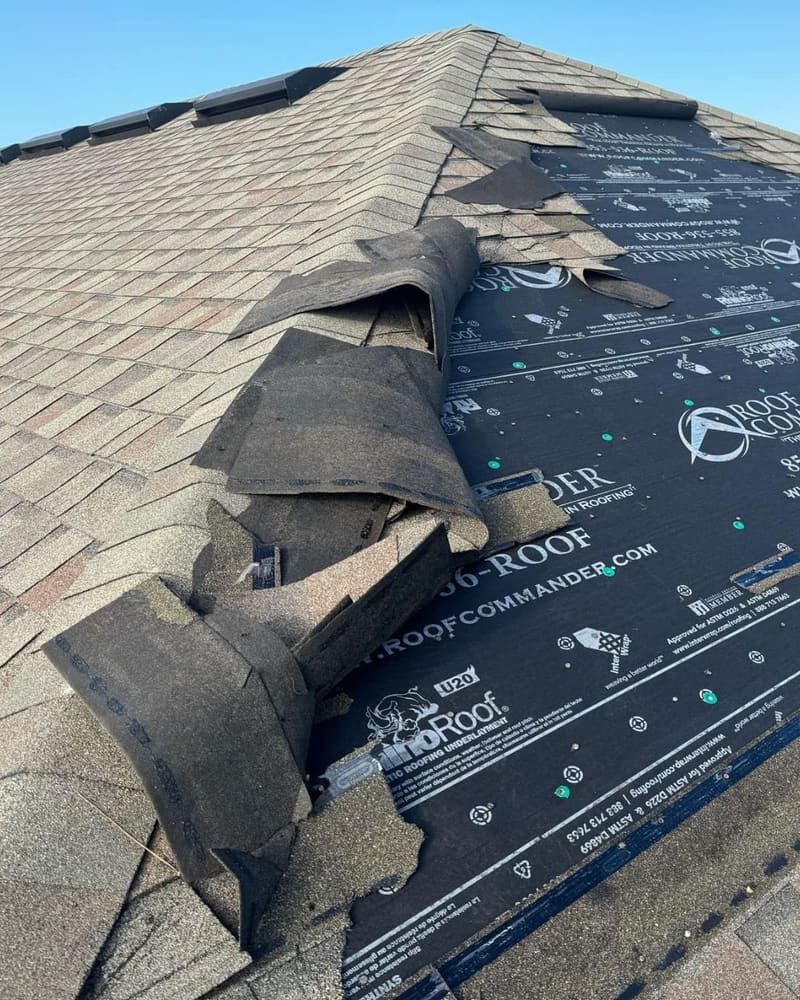 Storm damaged shingle roof with exposed roofing underlayment